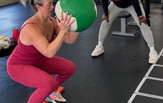 1. Personal trainer assisting woman with medicine ball exercise in gym setting.