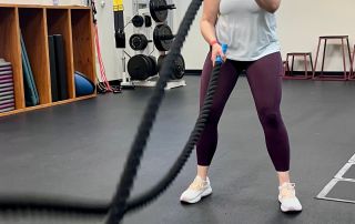 High-energy woman engaging in one-on-one fitness training with battle ropes at an indoor gym.