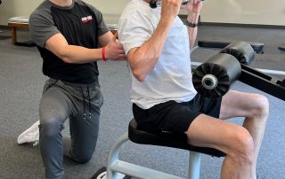 1. Personal trainer assisting elderly man with strength training at gym.