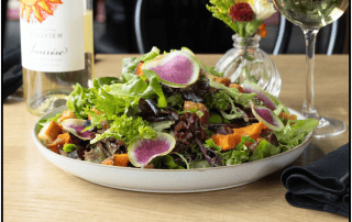 Fresh garden salad with mixed greens, radishes, and grilled vegetables, served on a white platter.